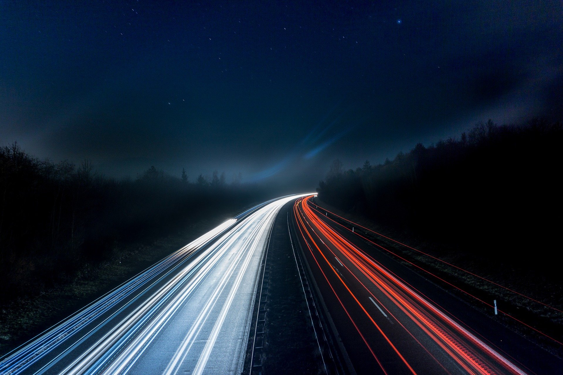 Lichtspuren vorbeifahrender Fahrzeuge auf einer Autobahn bei Nacht